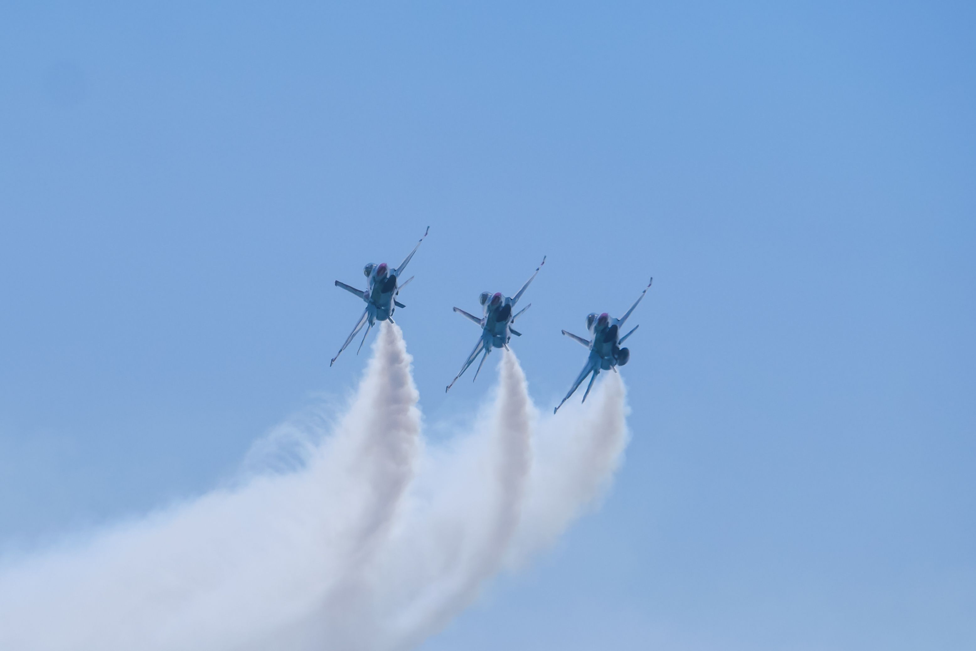 Three fighter jets fly in formation toward the camera with smoke trailing behind.