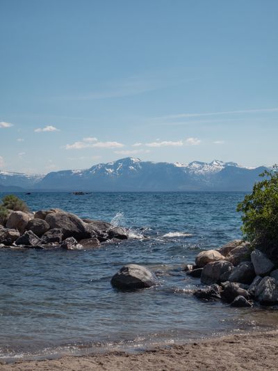 Lake Tahoe with rocks in the foreground gently being splashed by water with mountains visible in the background.
